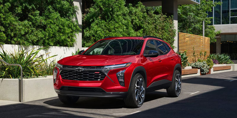 A red Chevrolet Trax parked in an urban setting with greenery in the background.