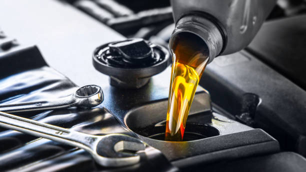 Motor oil being poured into a car engine, with wrenches nearby.
