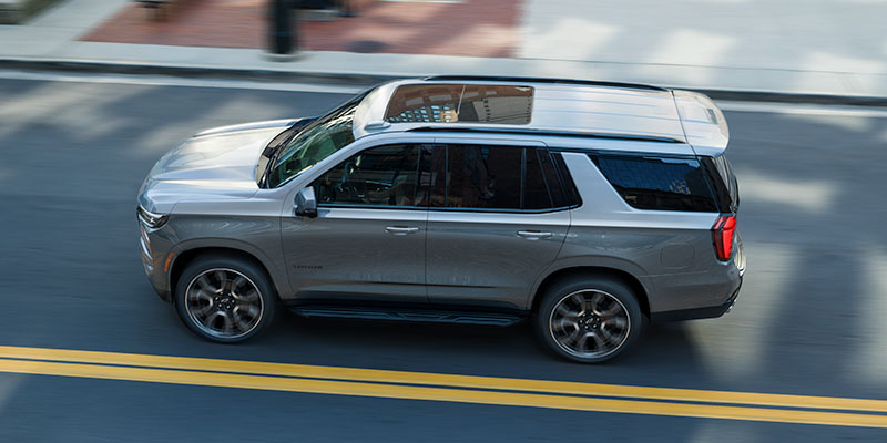 Silver Chevrolet Tahoe driving on city street from side view